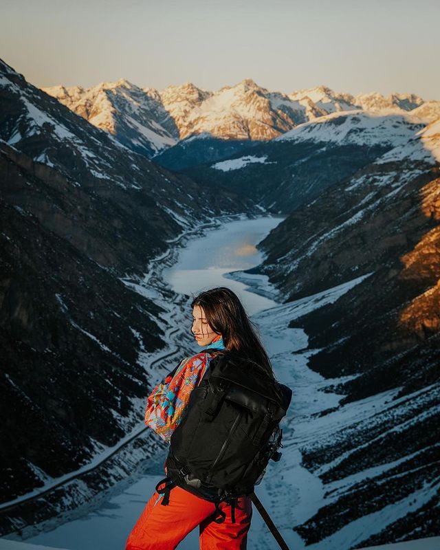 A woman with a waterproof travel backpack stands in front of a mountain range