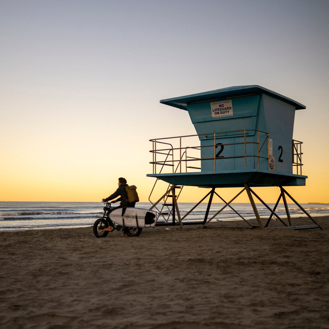 A man riding onto a beach with a surfboard and waterproof travel backpack