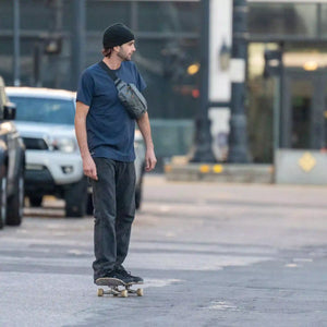 A man rides his skateboard through the city with his Rennen X-Pac Crossbody.