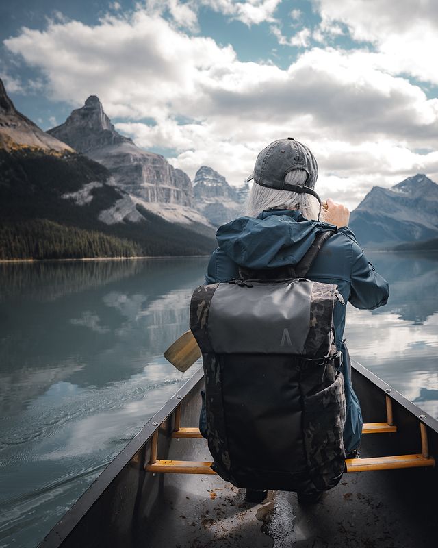 A woman with a waterproof travel backpack canoeing on a lake surrounded by mountains