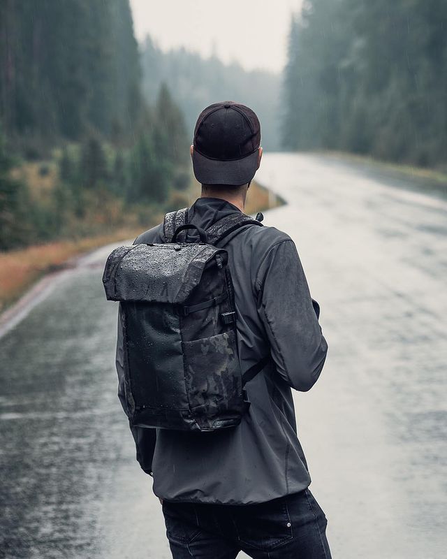 A man with the Errant Back waterproof travel backpack facing away from the camera in a rainstorm in the mountains