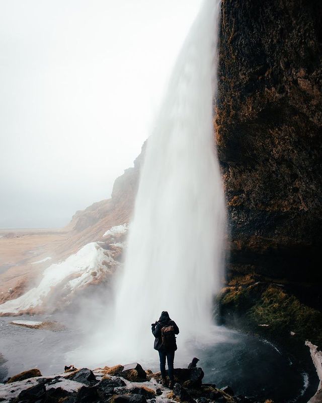 A person with a waterproof camera backpack standing in front of a waterfall