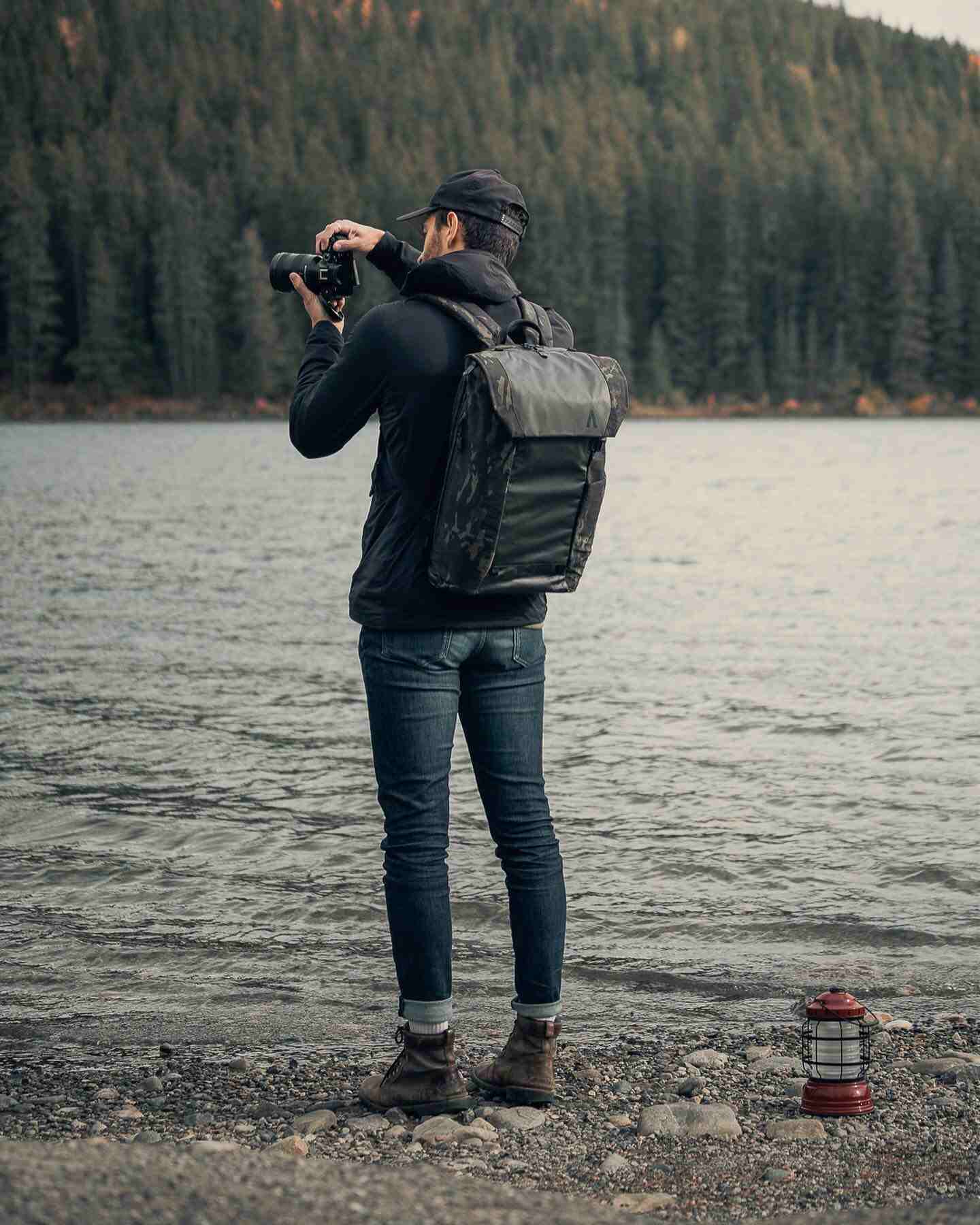 A man wearing a waterproof travel backpack taking photos by a lake