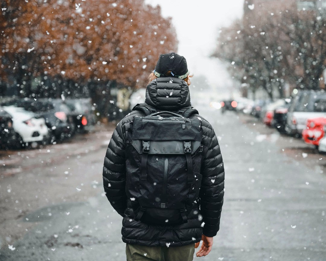 A man with a waterproof camera backpack walking in a snowy parking lot