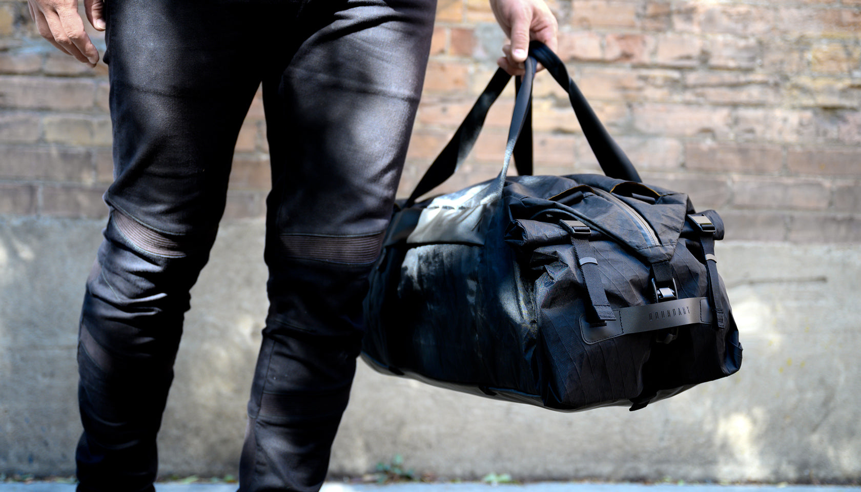 A man carrying his Duffle Pack X-Pac near a brick wall