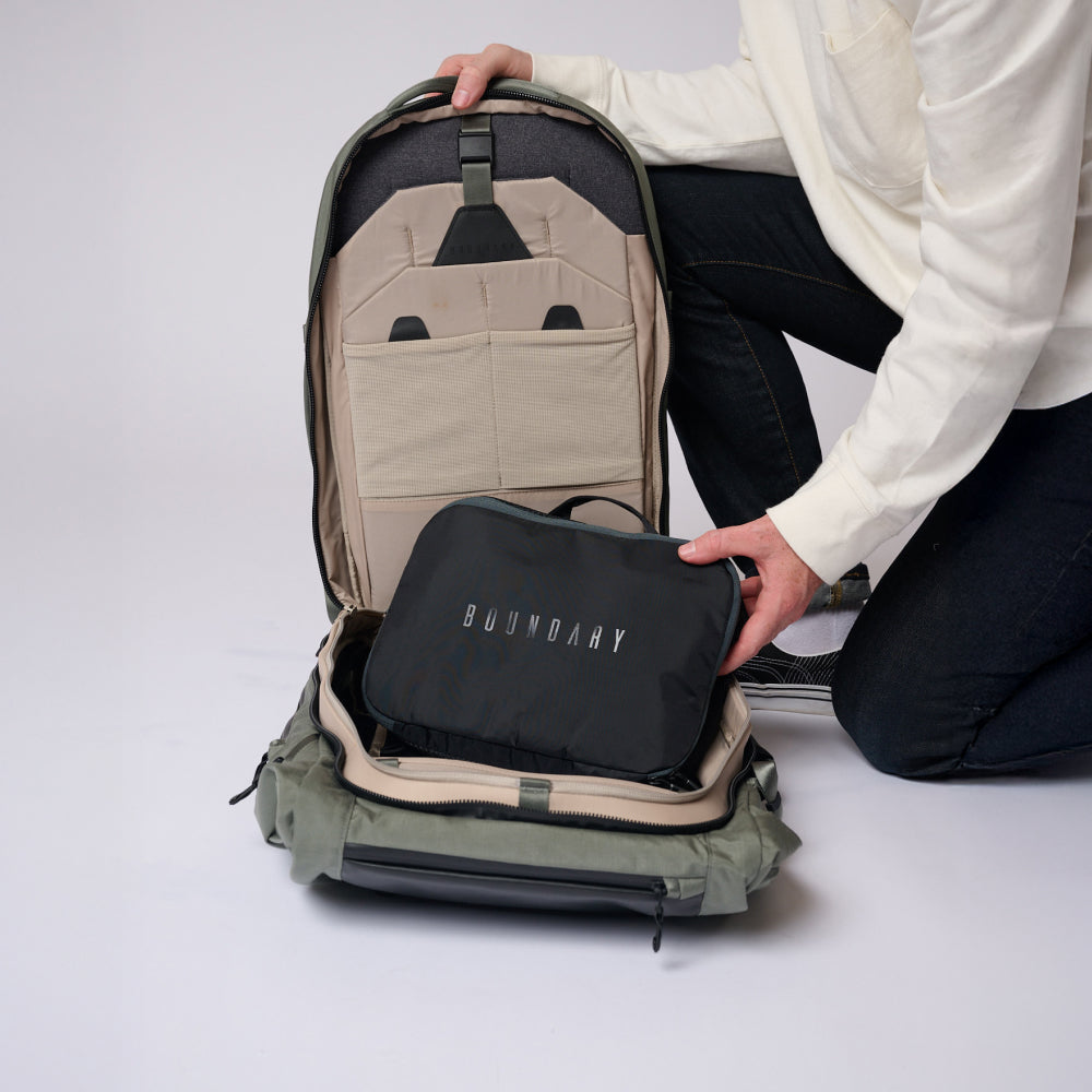 Person opening a green backpack to reveal a black pouch with 'Boundary' branding on a white background.