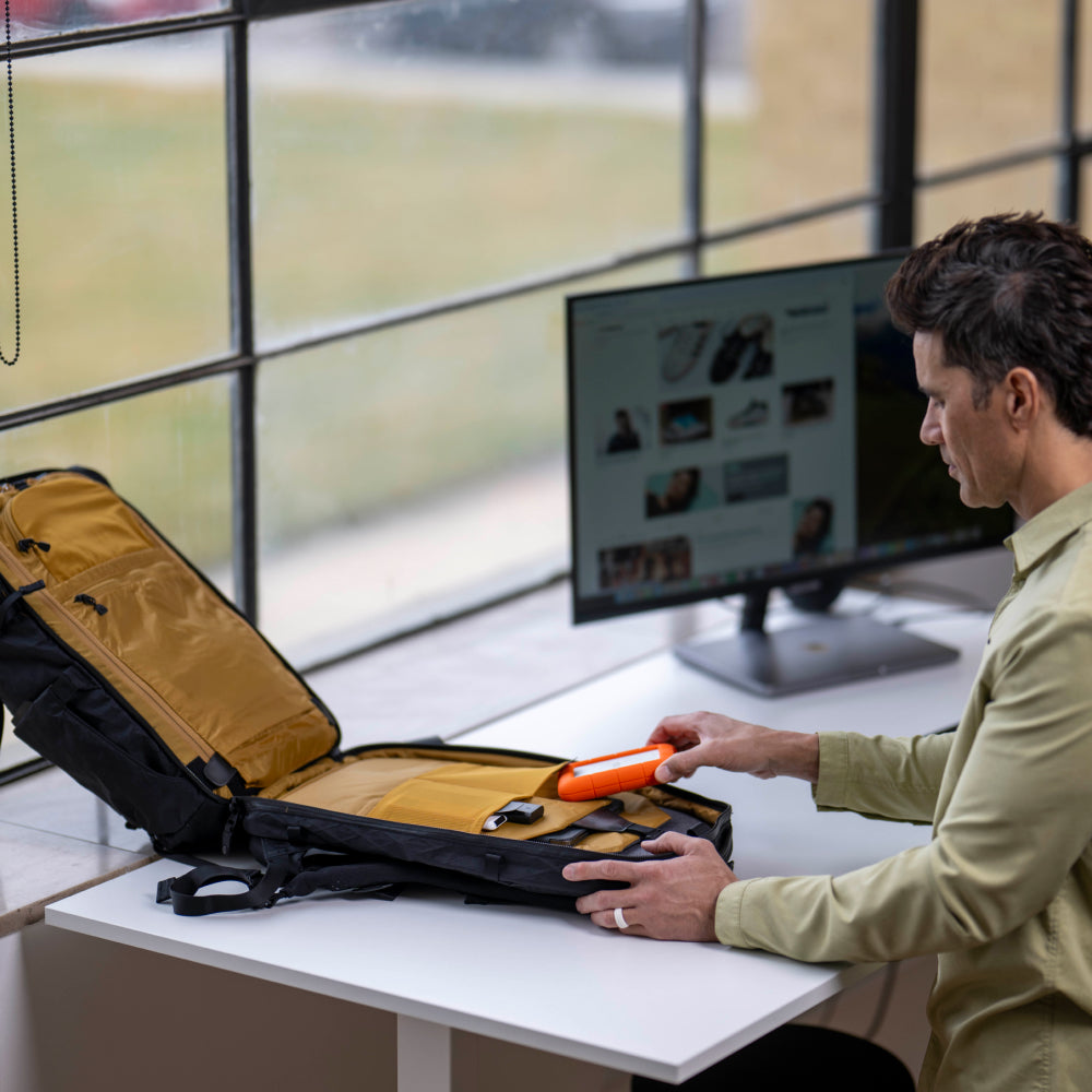 Man sitting at a desk with an open suitcase and a computer monitor displaying a webpage.