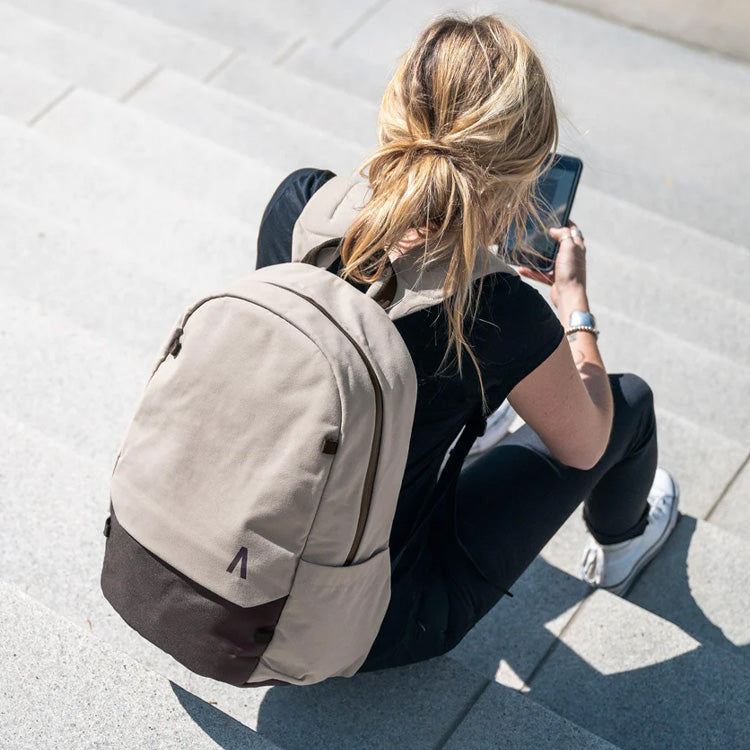 A woman, with a Boundary Supply backpack, sitting on some steps while looking at her phone.