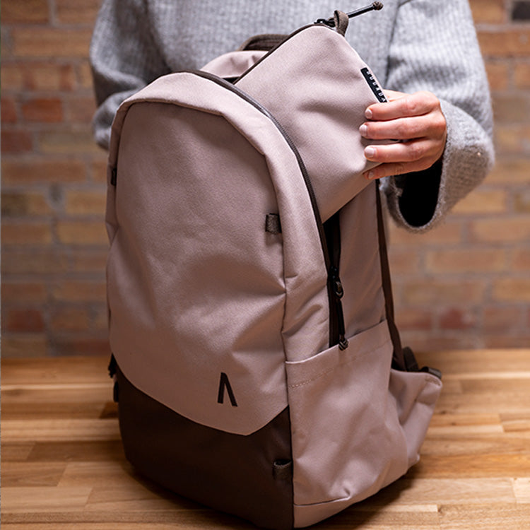 A young woman inserts a small case into her Rennen Recycled Daypack by Boundary Supply.