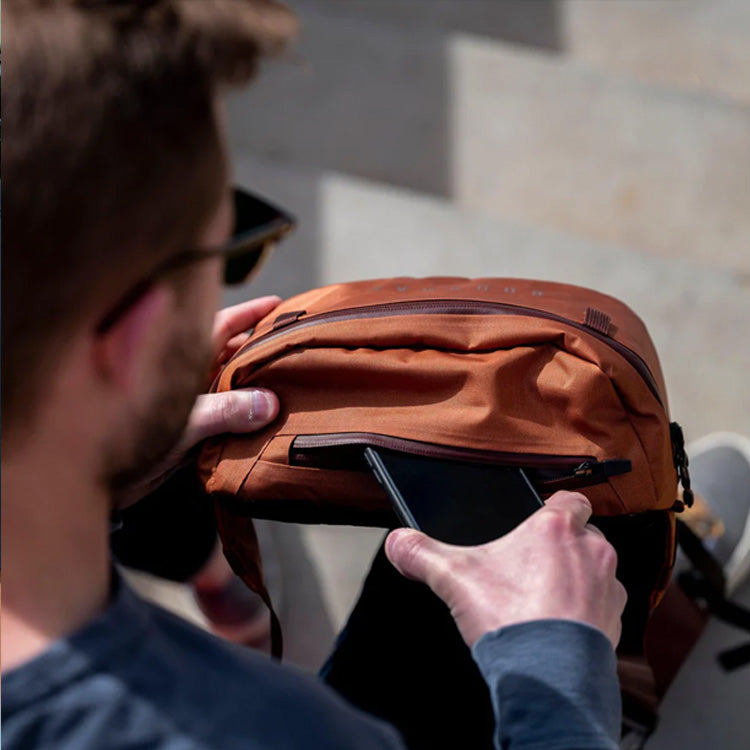A man slides his phone into a compartment on his Boundary Supply backpack.