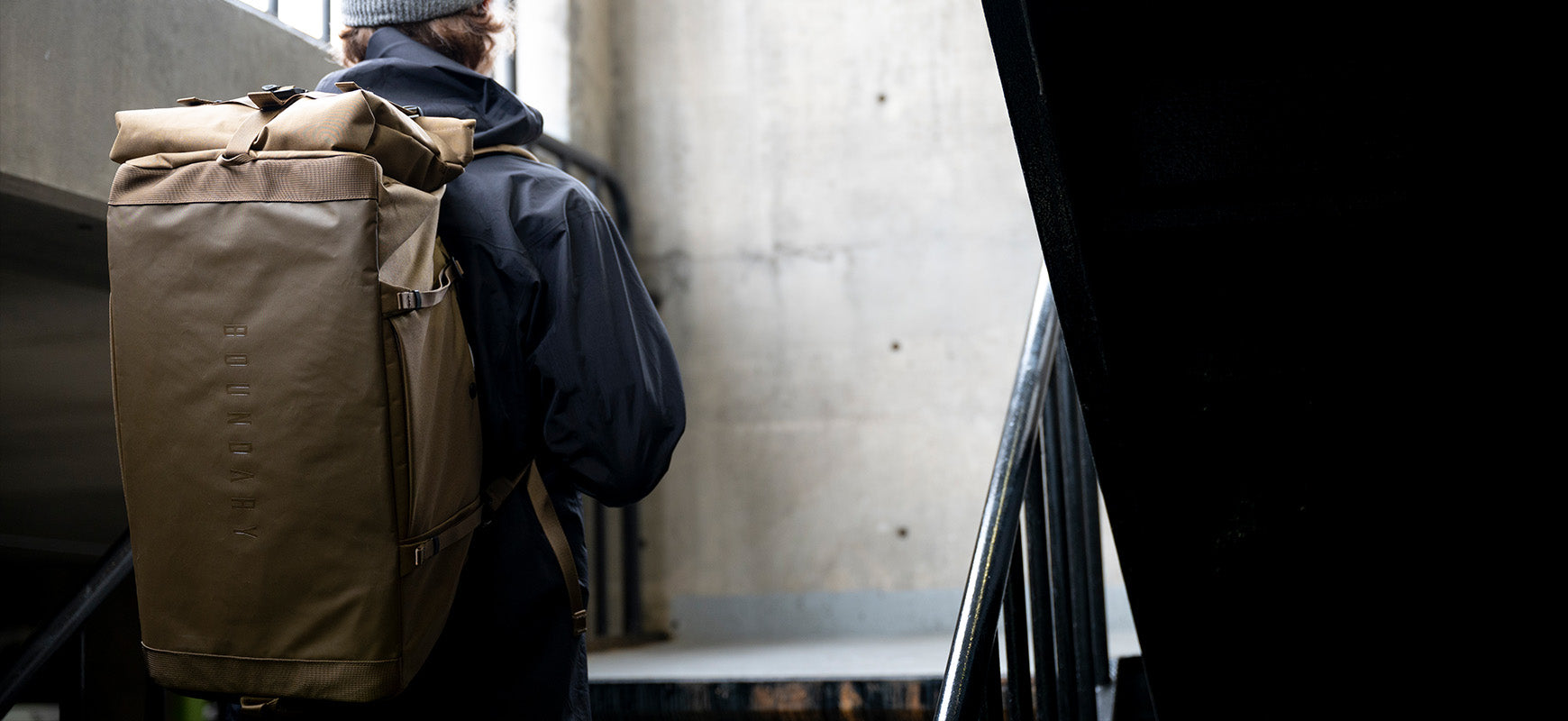 A man in a blue jacket climbs a stairway with his Boundary Supply travel backpack.