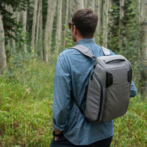 Man wanders through a forest with his gray Boundary Supply backpack.