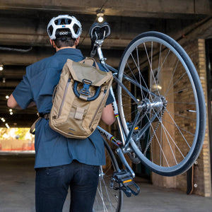 A man carries his bike with a Boundary Supply backpack strapped to his back.