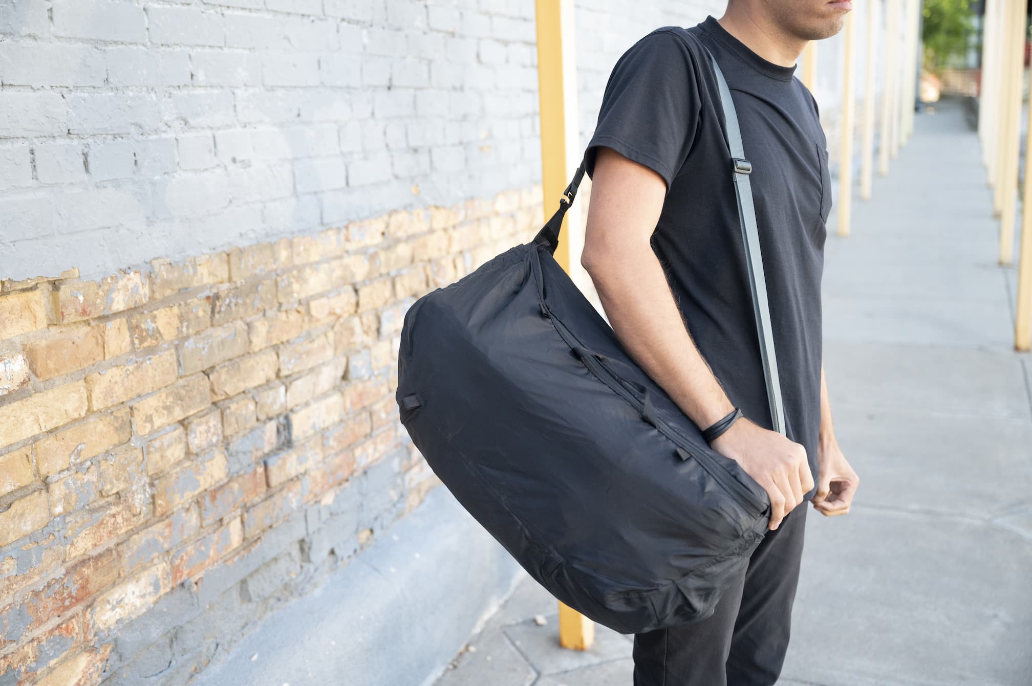 A man waits along a sidewalk with a Boundary Supply waterproof duffel strapped over his shoulder.