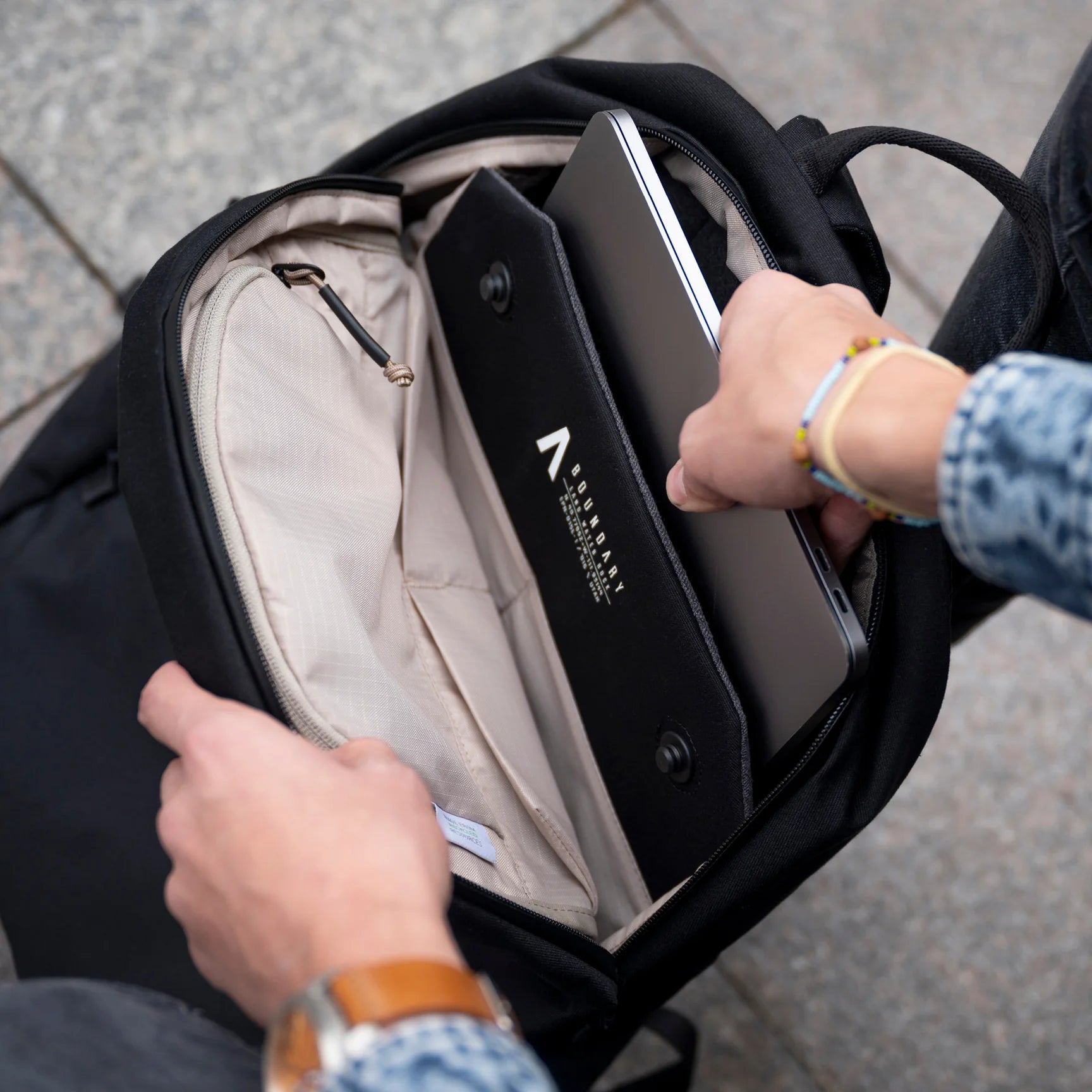 A man pulling out his laptop from his Obsidian Rennen Recycled Daypack by Boundary Supply.