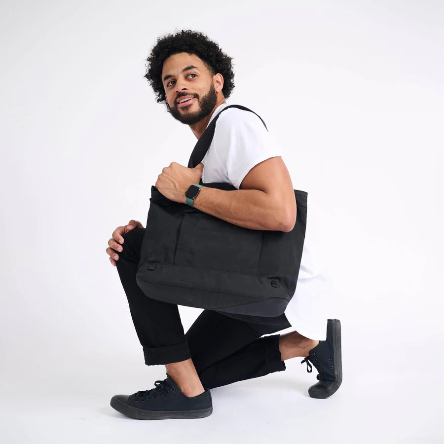 A man kneeling on one knee with his Rennen Tote bag from Boundary Supply