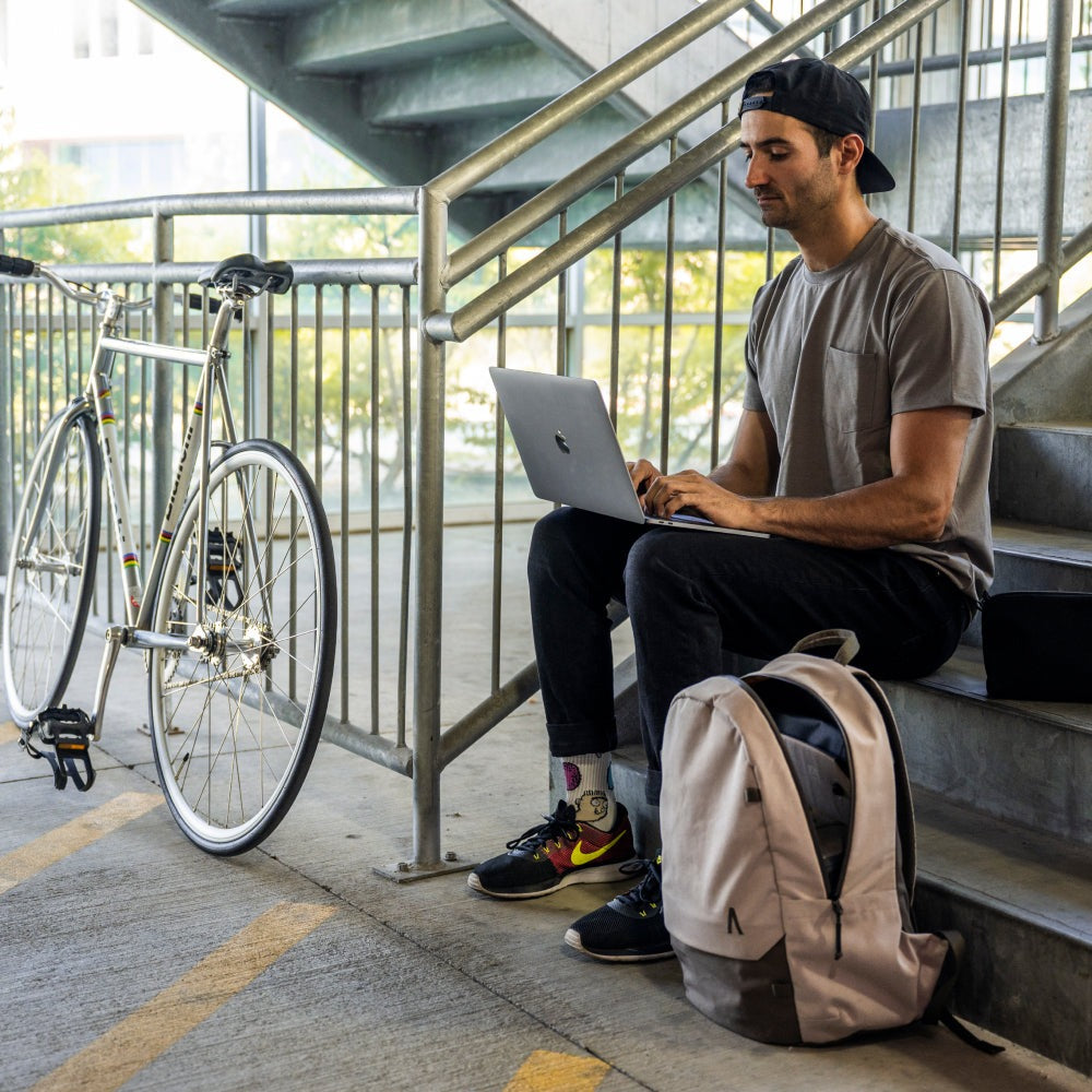 Man using a laptop on a staircase with a bicycle and backpack nearby