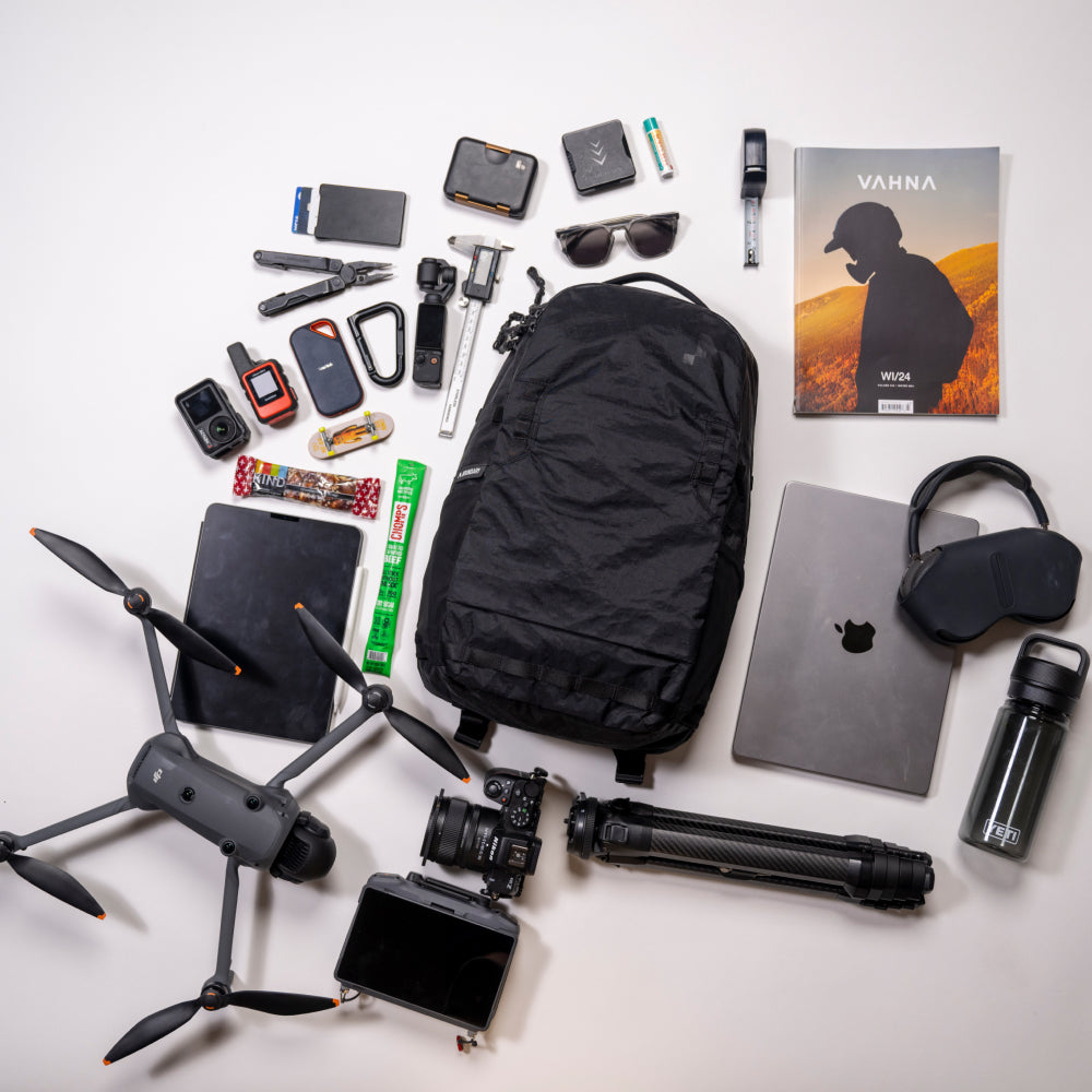 Collection of travel items including a backpack, drone, camera, and electronic devices on a white background.
