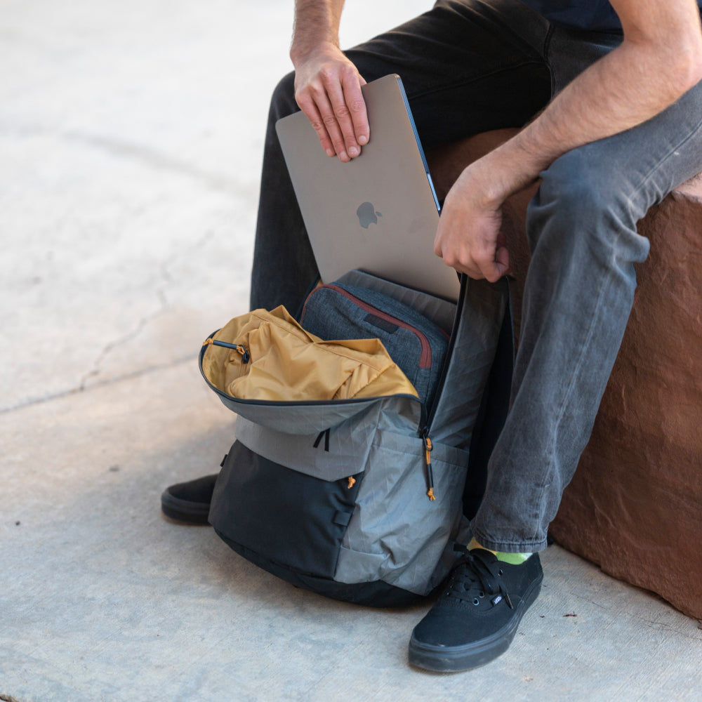 Person sitting on a rock with a backpack open, revealing a laptop and other items.