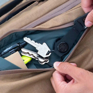 An individual stashes their keys, pens, and other miscellaneous items in a small compartment of their Errant Pack.