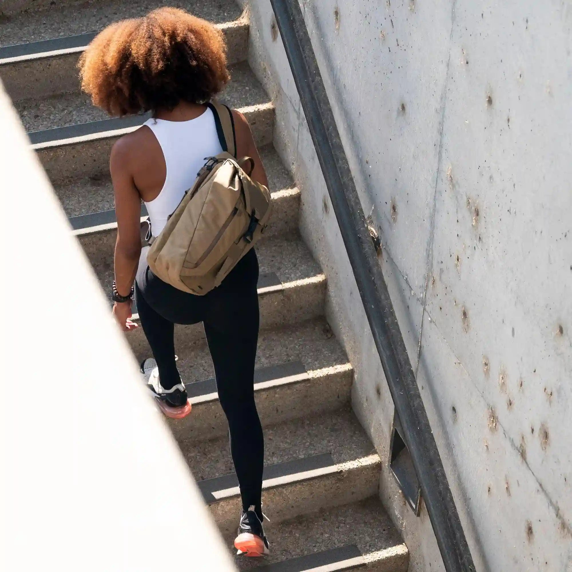 A young woman climbs some stairs with her Errant Sling strapped across her back.